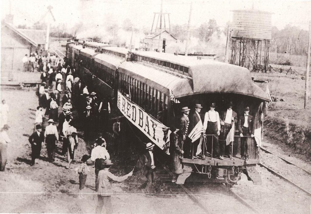 Super Old Picture of train with Red Bay banner on side.